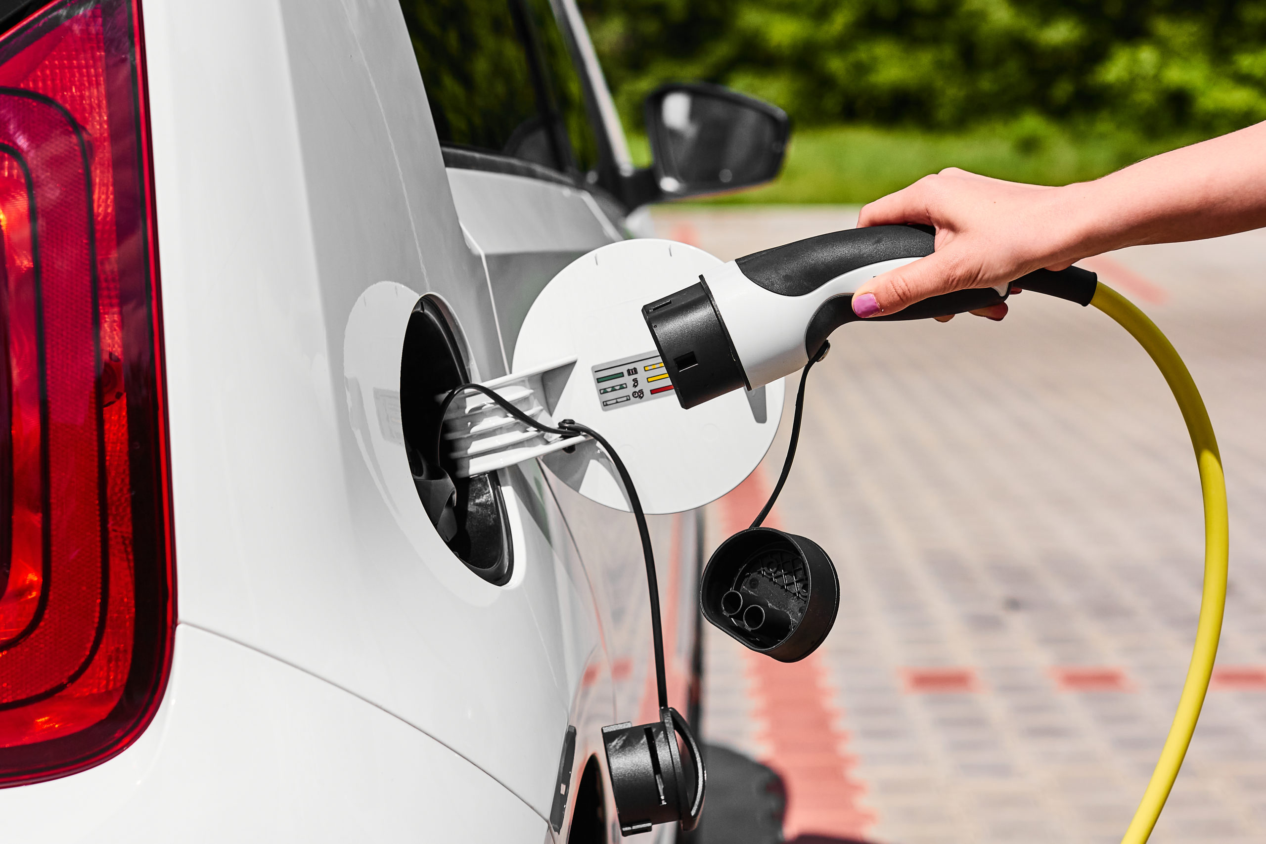 Close up woman hands plugging a power supply cable to electric car for charging at charging station outdoor